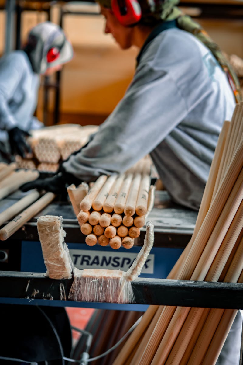 Industrial workers operating machinery for processing wooden rods in a factory setting.